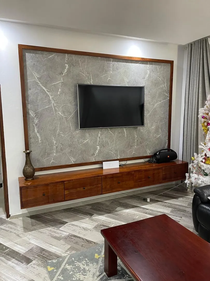 Marble-pattern TV panel with a wood frame above a floating wooden cabinet with drawers